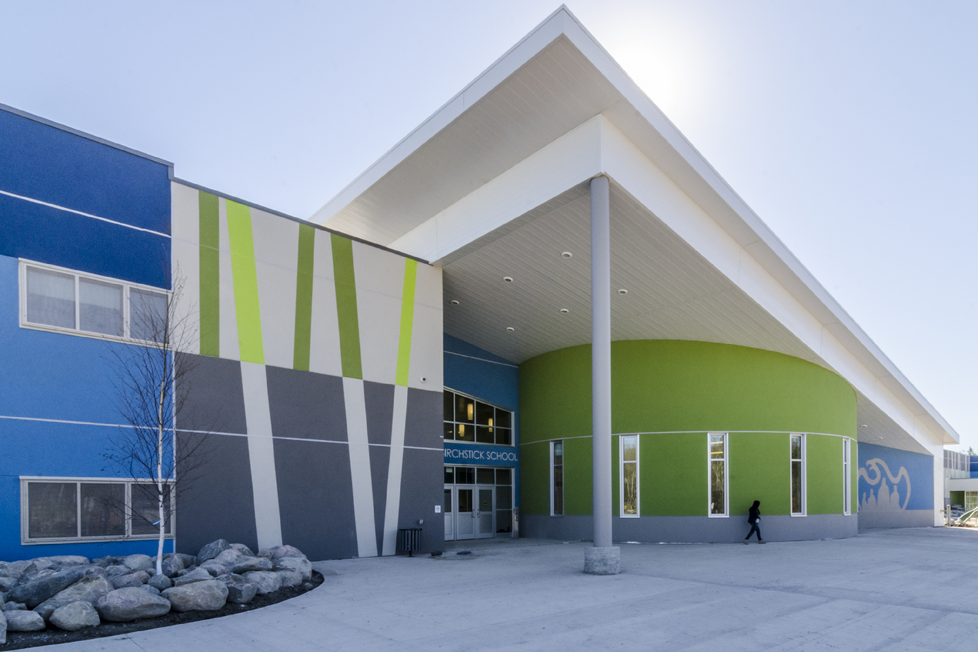 Large two-storey blue, grey, and green stucco building with a large, angled canopy stretching over the entrance.